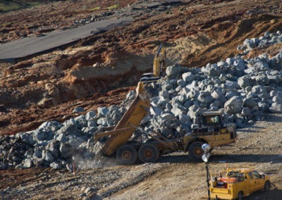 Large dump trucks unload rock to shore up erosion control on emergency spillway.