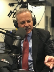 Mark Ghilarducci wearing headphones and talking into a microphone