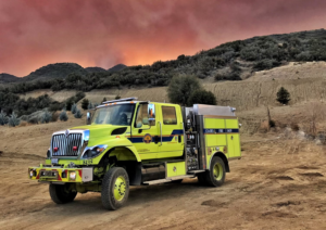 Cal OES fire truck parked in front of a hill on the scene of a fire.