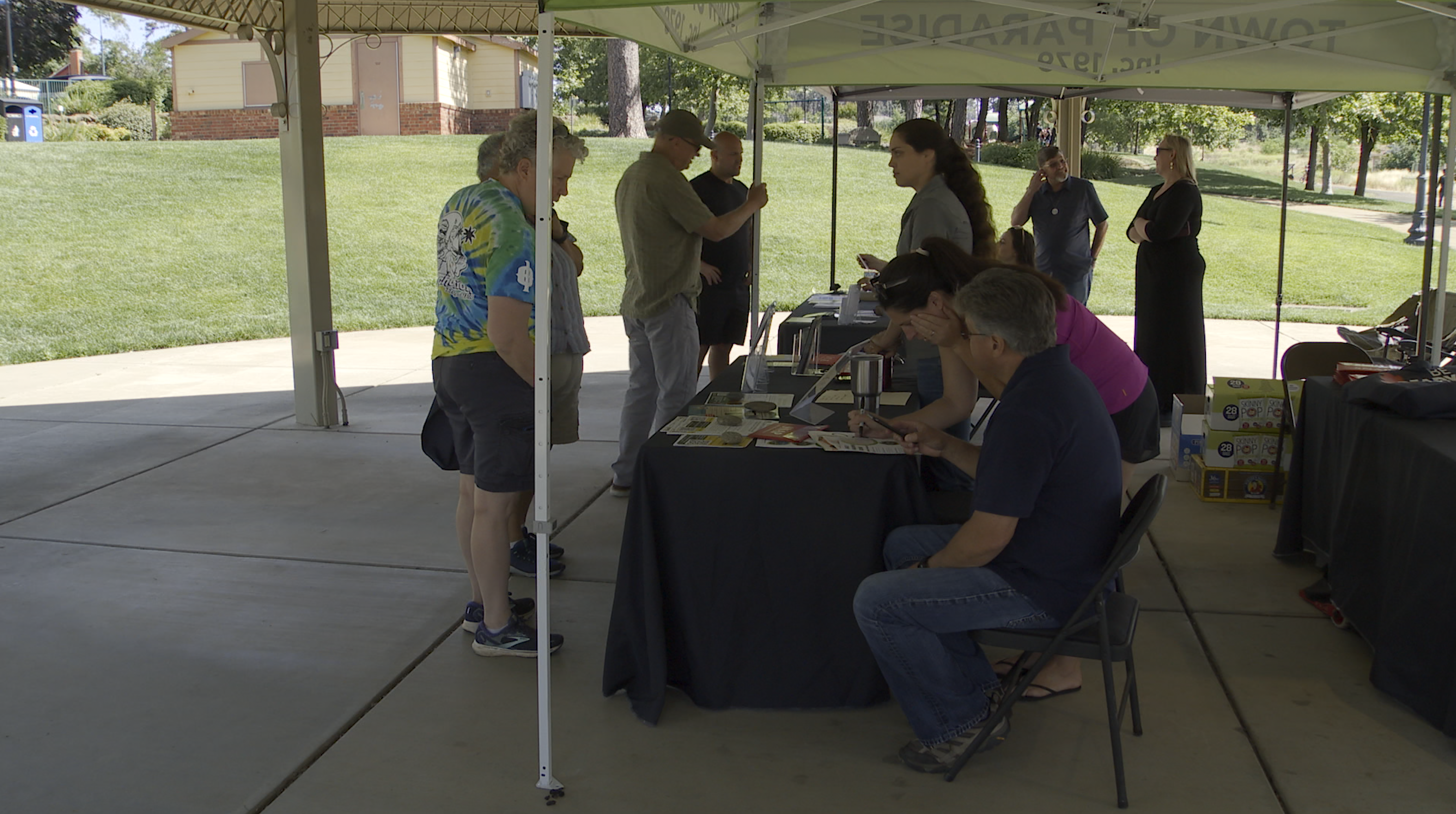 Paradise, California residents under a pop-up tent looking at wildfire preparedness materials, including pamphlets, brochures, and emergency supplies.