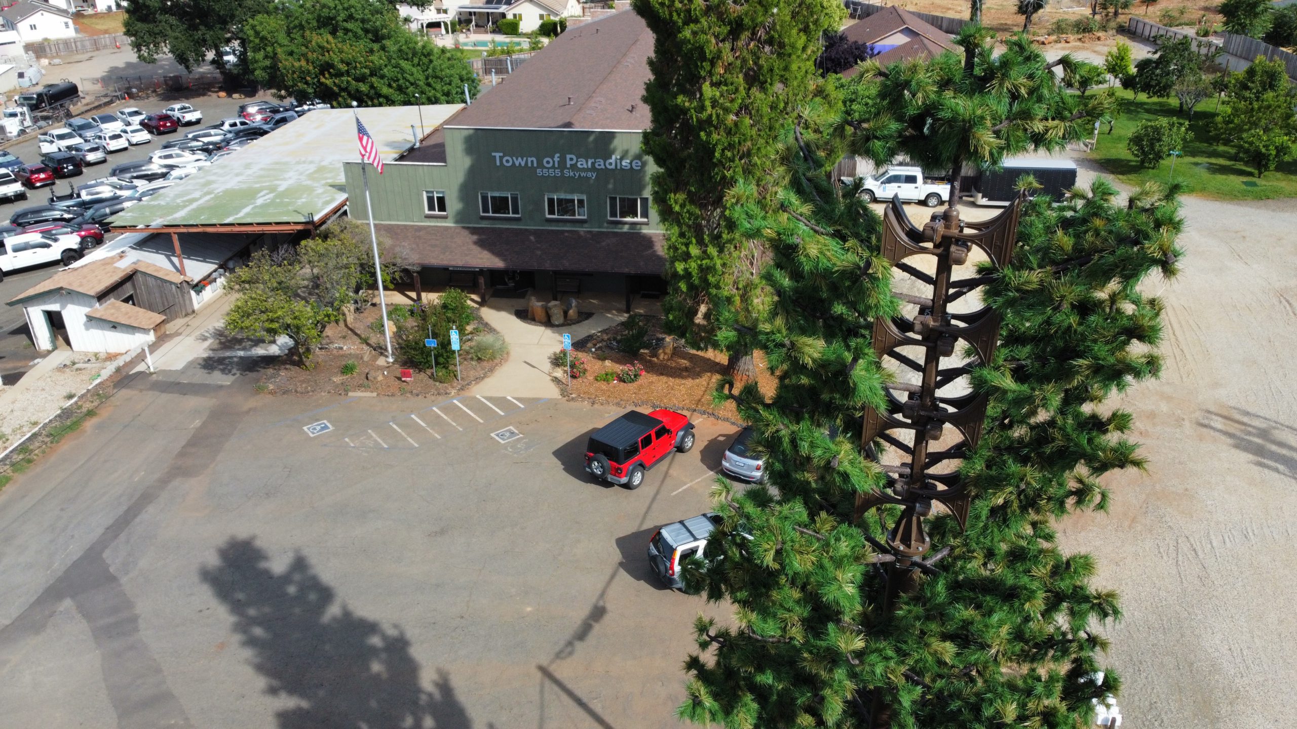 Early Warning Siren tower in front of Paradise townhall in Paradise, California. The tower is brown metal with various megaphones on it, covered in realistic tree branches.