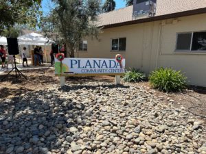 Image of the Planada Community Center sign outside of a building with people gathering in the background