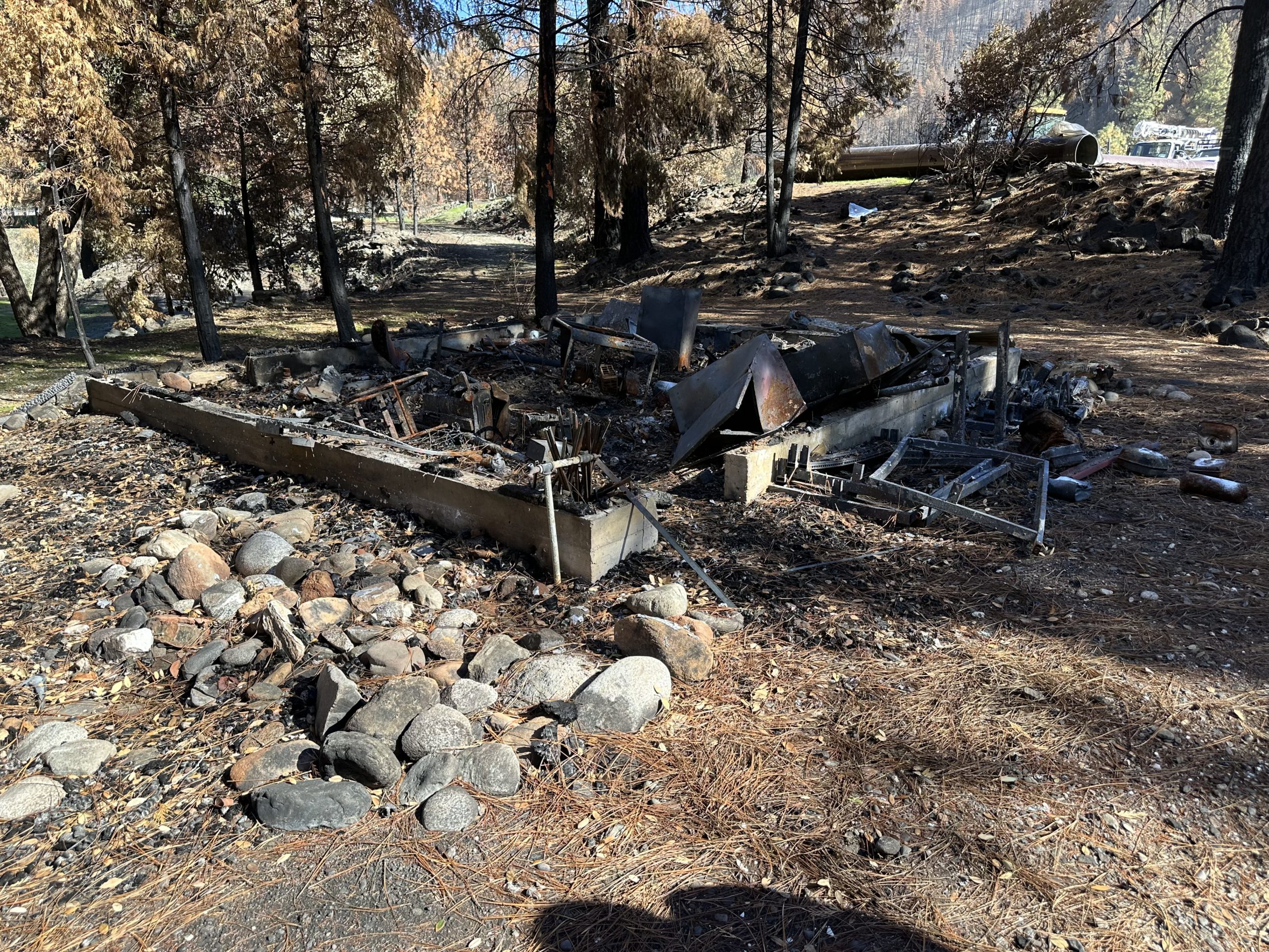 A burned structure base surrounded by tall pine trees.