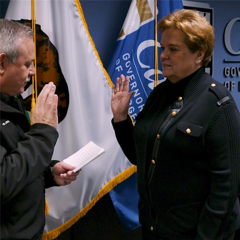 Cal OES Director Nancy Ward getting sworn in, with her right hand raised. There are California and Cal OES flags in the background.