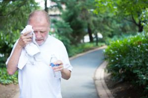 an elderly man walking, sweating and wiping forehead while holding a bottle of water