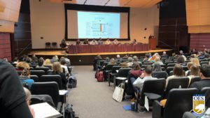 image of auditorium with presenters sitting at a table