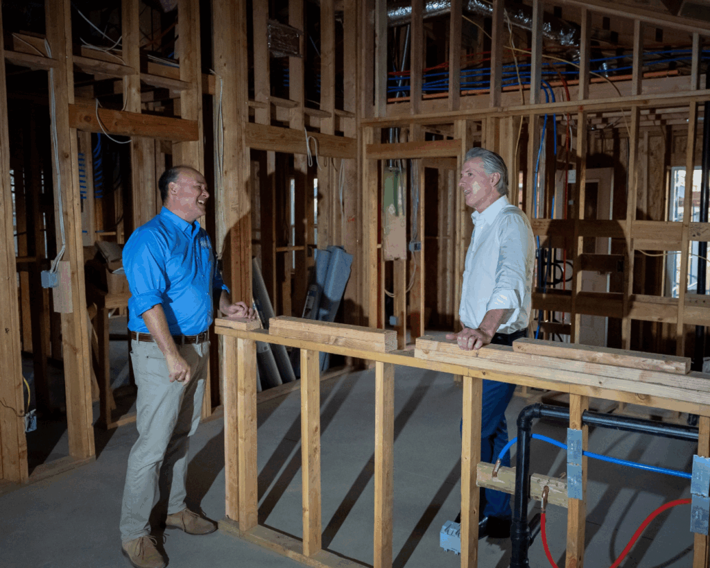 Governor Newsom stands in a building under construction talking to the CEO of Habitat for Humanity of San Gabriel.